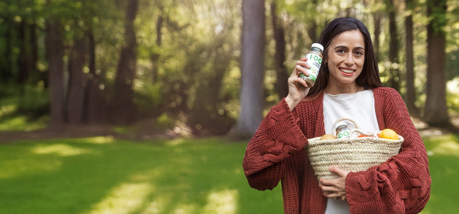 Ein Mädchen hält eine Flasche Bio-Kaltpresssaft von I·DO und eine Tasche voller Bio-Gemüse und -Obst.