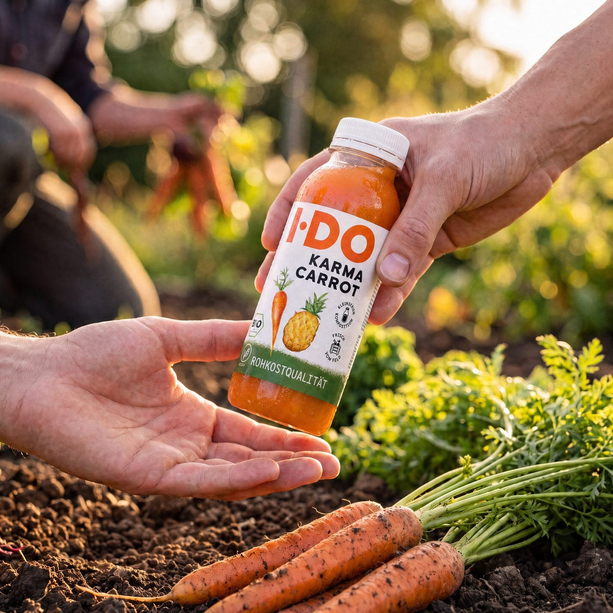 Eine Hand reicht eine I·DO Karma Carrot Flasche an eine offene Hand weiter – Übergabe im goldenen Abendlicht auf dem Feld